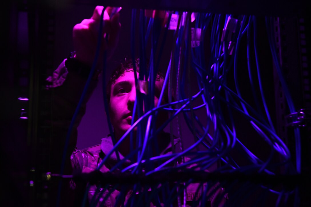 An airman works with wiring in a darkened room.