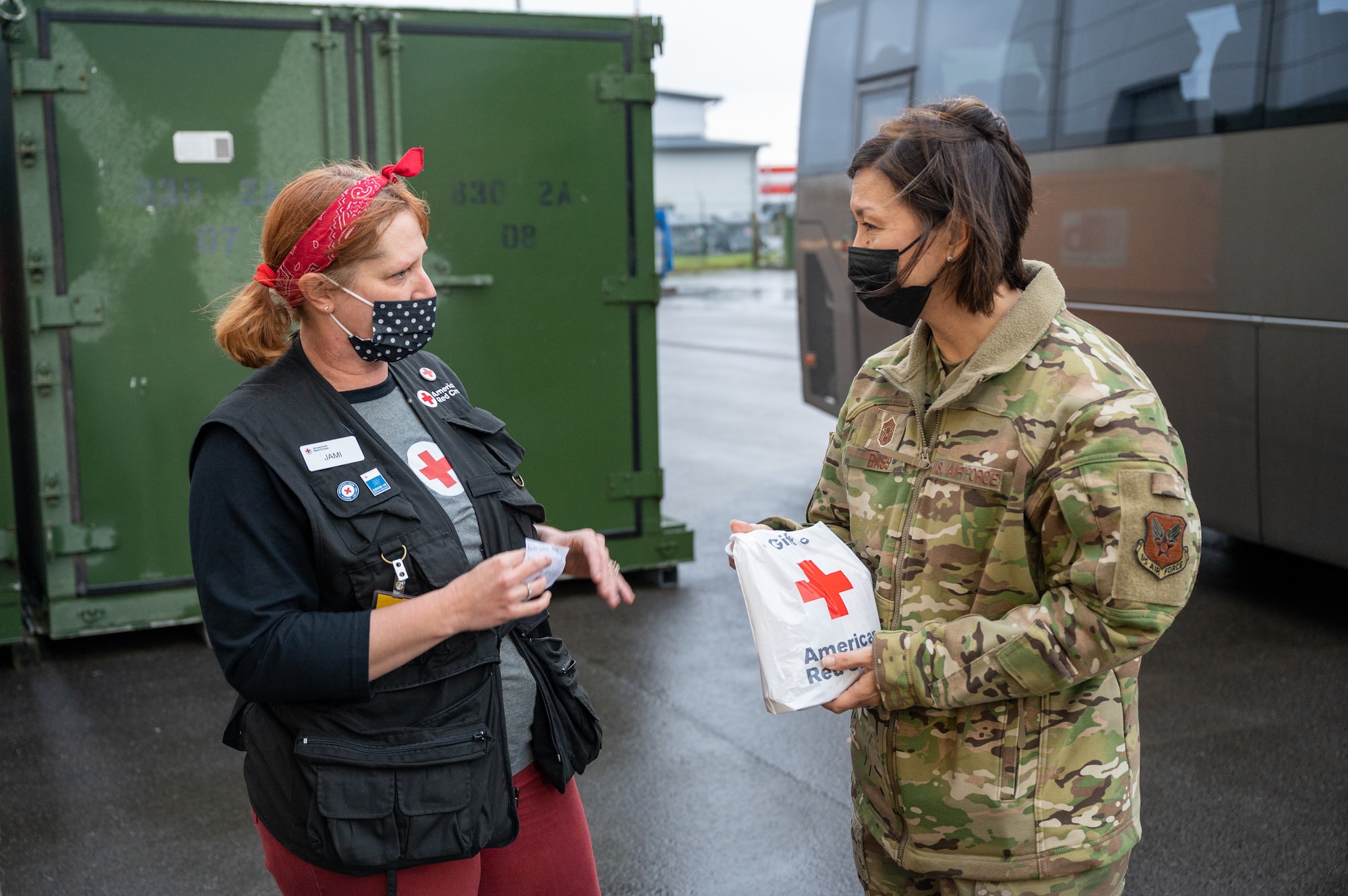 A volunteer and a military member standing outside next to a bus.