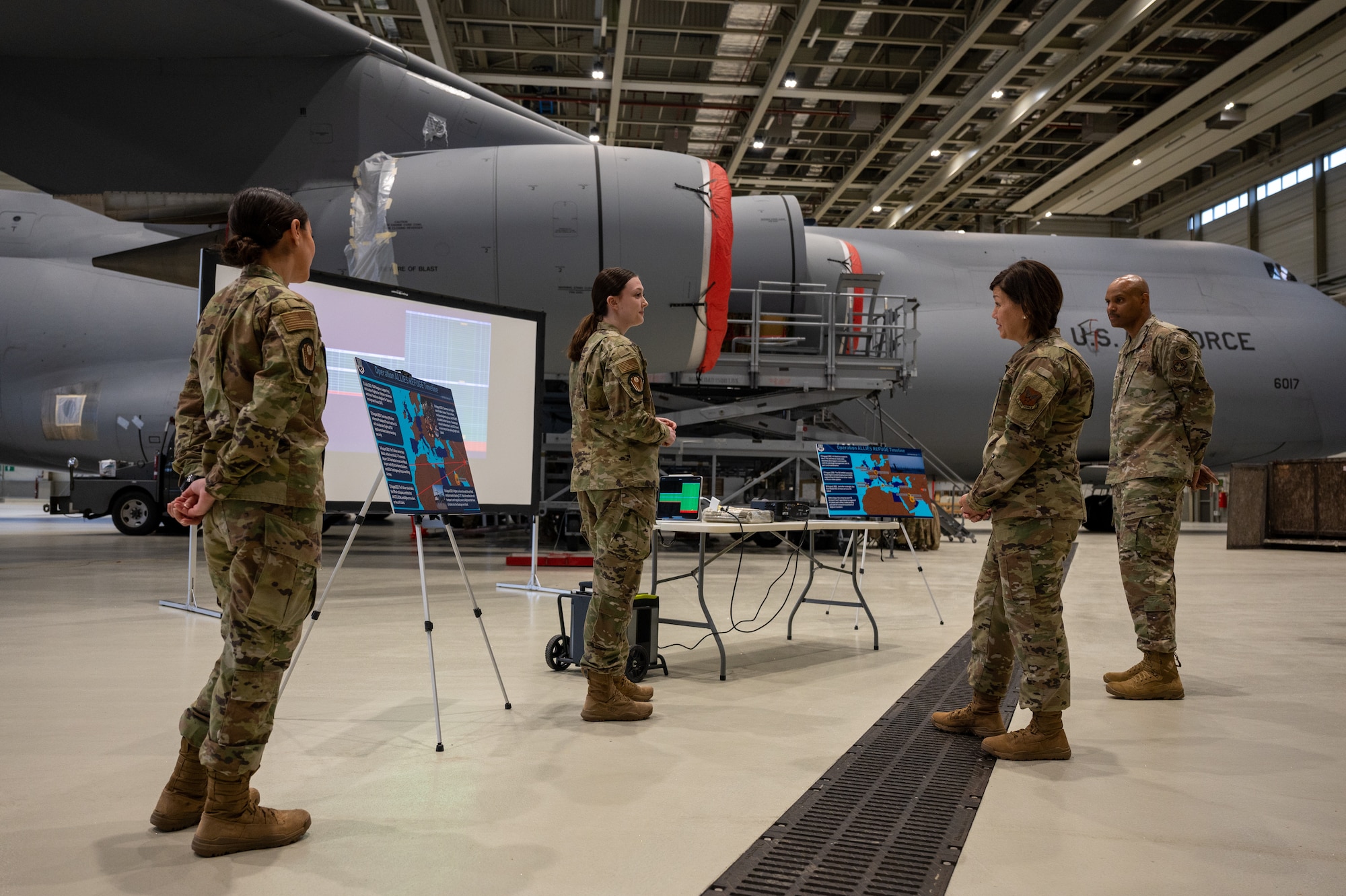 A group of military members standing in a hangar with an aircraft.
