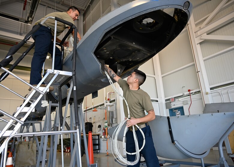 Staff Sgt. Jason Ayala (right) passes wiring through the MQ-9 Reaper to Staff Sgt. Paul Robledo Garcia (left). Both are 214 LRE Avionics Technicians here, and some of the first Air National Guard and Air Force maintainers to completely dis- and reassemble the aircraft.