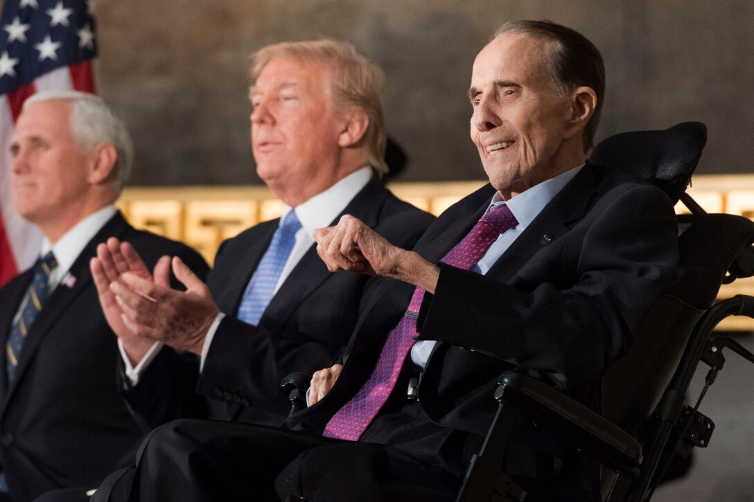 Three men in suits sit together while reacting to a speech.