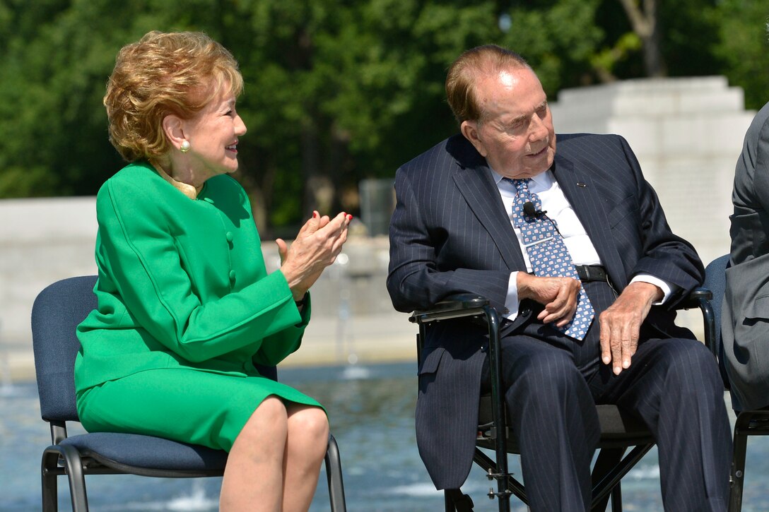 Woman wearing green dress applauds a man seated beside her.