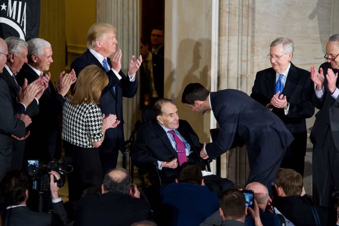 Government leaders applaud Sen. Robert Dole, who is seated in a wheelchair among them.