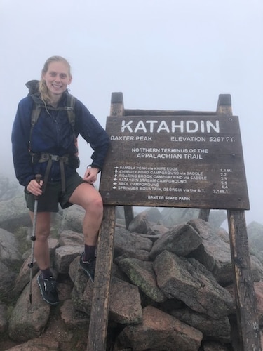 Hiker takes photo in front of sign on mountain.