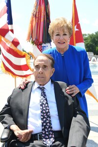 Woman stands behind a seated man as they pose for a photo.