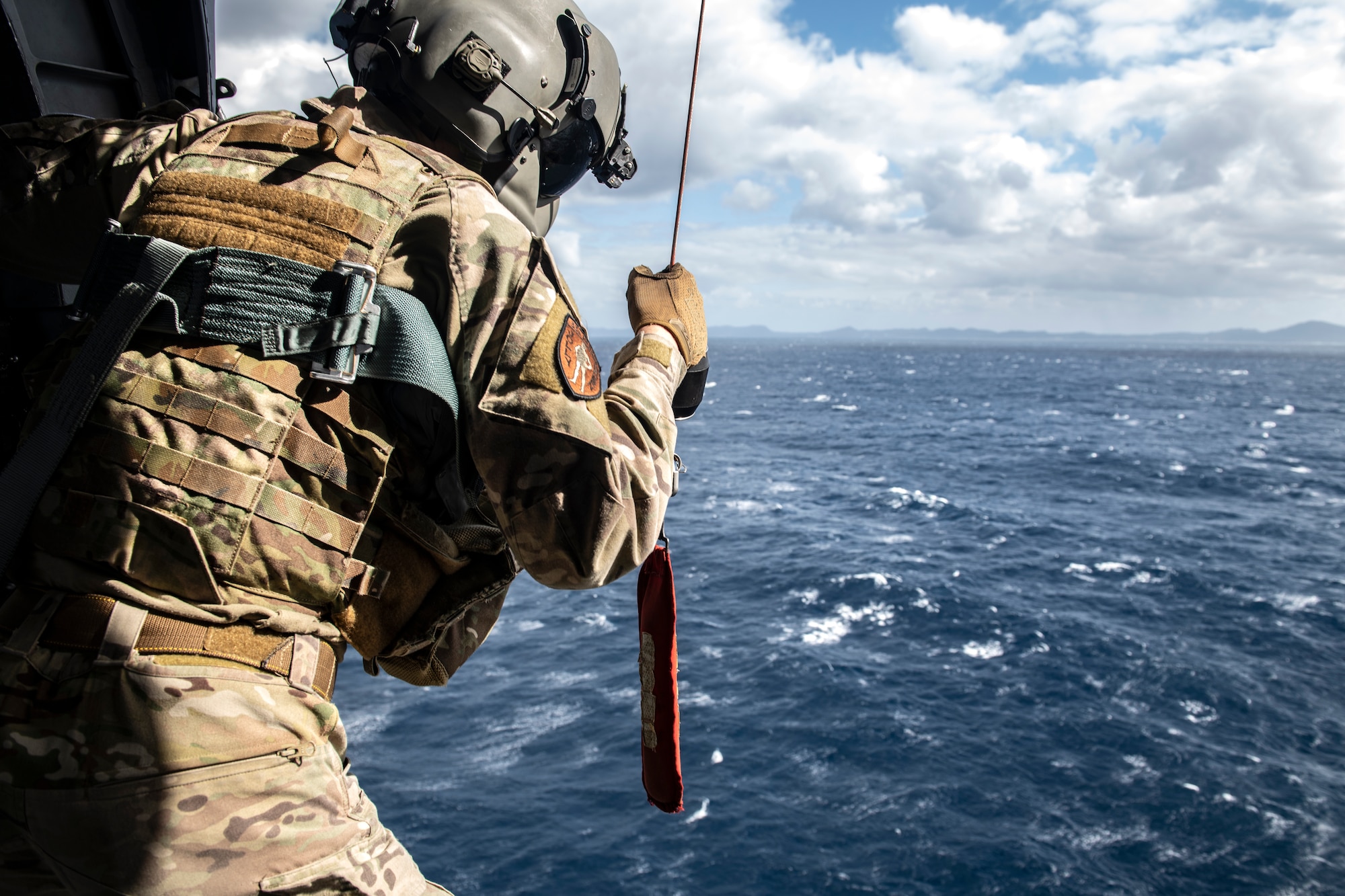 Senior Airman Tanner Cornell, 33rd Rescue Squadron special missions aviator, readies the hoist to be lowered from an HH-60G Pave Hawk during daytime water rescue operations over the Pacific Ocean, Dec. 1, 2021. The Pave Hawk is equipped with a hoist capable of lifting up to 600 pounds during personnel recovery operations. (U.S. Air Force photo by Senior Airman Jessi Monte)
