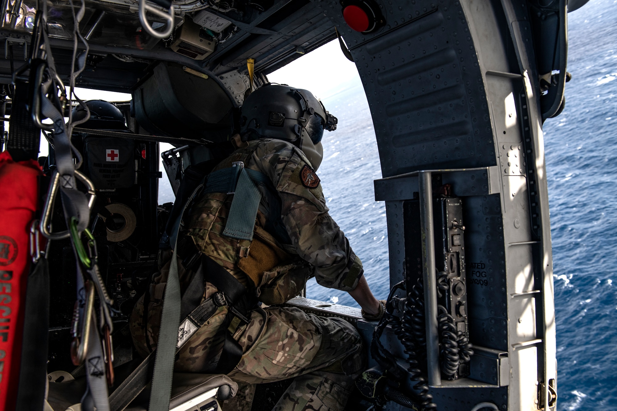 Senior Airman Tanner Cornell, 33rd Rescue Squadron special missions aviator, looks out the window of an HH-60G Pave Hawk during daytime water rescue operations over the Pacific Ocean, Dec. 1, 2021. The 33rd RQS maintains readiness for mobilization, deployment and employment of helicopters and rescue of U.S. and allied military members, and civilian personnel. (U.S. Air Force photo by Senior Airman Jessi Monte)