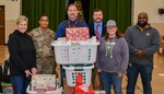 Six people next to a stack of Christmas gifts.