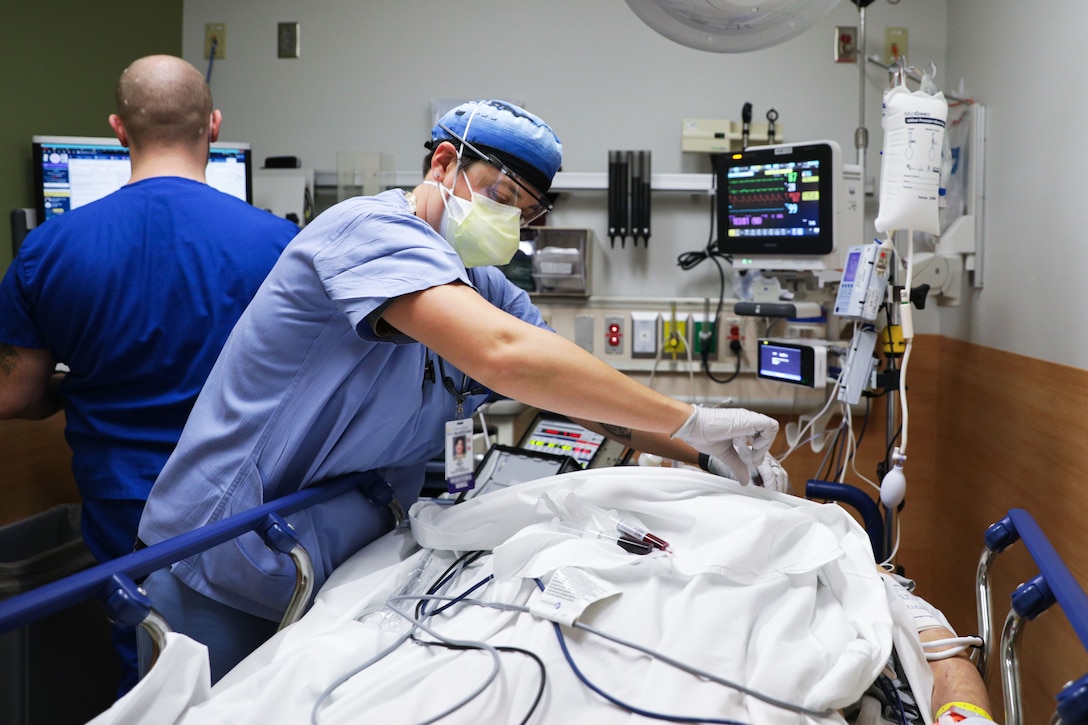 A male nurse wearing a face mask and gloves takes a patient’s blood.