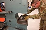 U.S. Air Force Master Sgt. Paul Allen, a structural maintainer with the 173rd Fighter Wing, places a part in the "smash-box," a reinforced steel container lined with thick, durable rubber that shapes the flat aluminum part when put under extreme pressure on Nov.5, 2021.