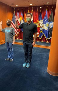 Man standing with is right arm raised in front of all military branch flags taking his Oath of Enlistment to join the United State Army.