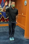 Man standing with is right arm raised in front of all military branch flags taking his Oath of Enlistment to join the United State Army.