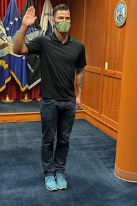 Man standing with is right arm raised in front of all military branch flags taking his Oath of Enlistment to join the United State Army.