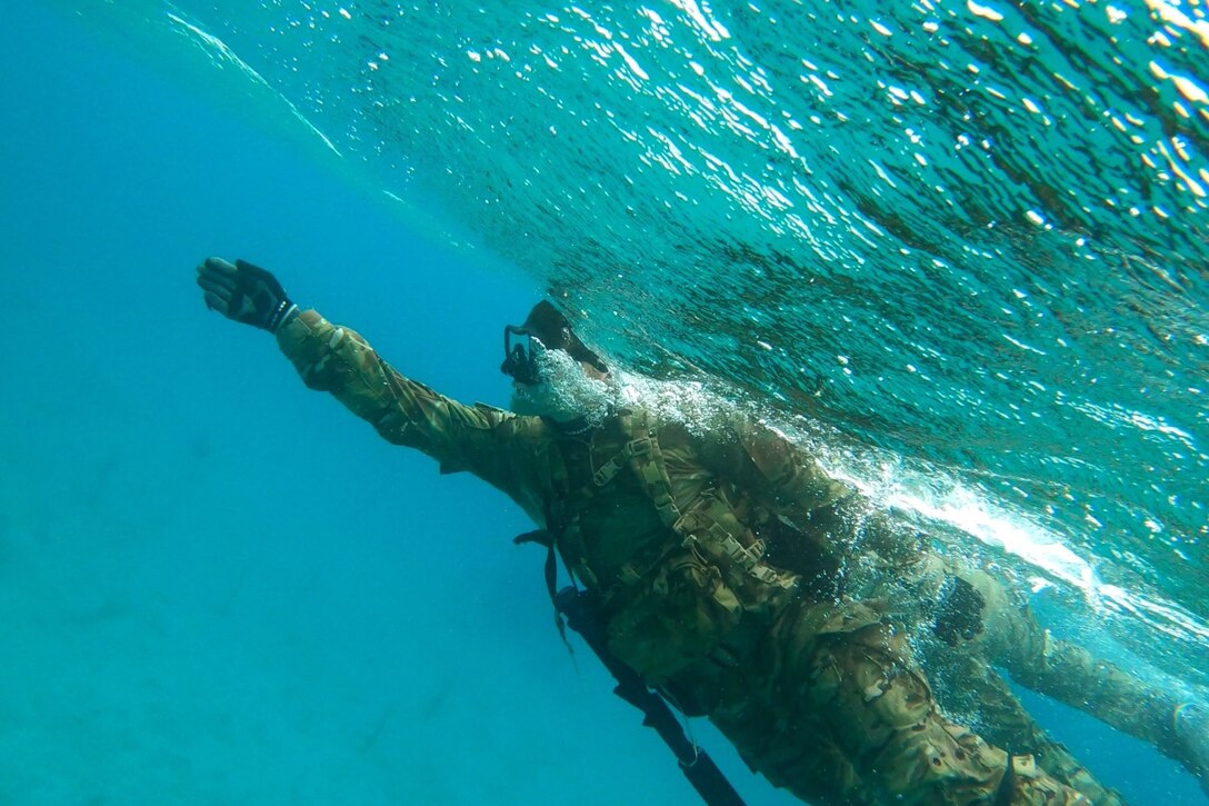 A soldier swims underwater.