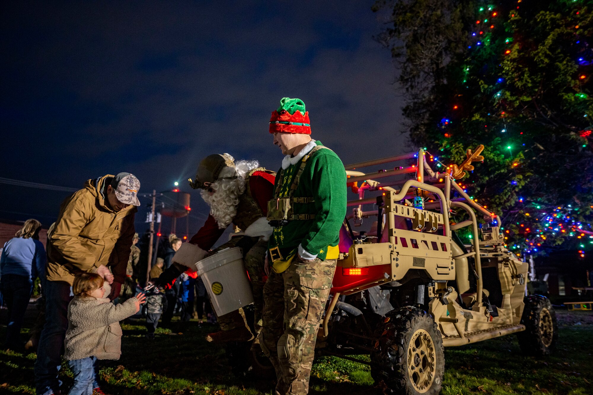 U.S. service members hand out candy canes to children at Joint Base Lewis-McChord, Washington, Dec. 2, 2021. The service members dressed up as Santa and his elf as part of a tree lighting ceremony at McChord Field. (U.S. Air photo by Airman First Class Charles Casner)