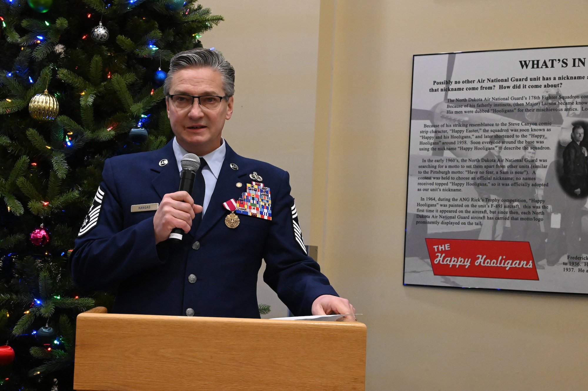 Chief Master Sgt. Duane Kangas stands at a podium and speaks to an audience using a microphone during his retirement ceremony at the North Dakota Air National Guard Base, Fargo, N.D., Dec. 4, 2021.