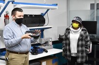 IMAGE: Michael Darnell (left), Innovation Lab engineer, explains a piece of virtual reality equipment to Andrea Clement, a member of the Colonial Beach town council in the Digital Warfare Innovation Center Lab as part of a tour with local elected officials. During their visit, the local officials received a briefing on multiple program areas and visited the Digital Warfare Innovation Center Lab and the laser lab.