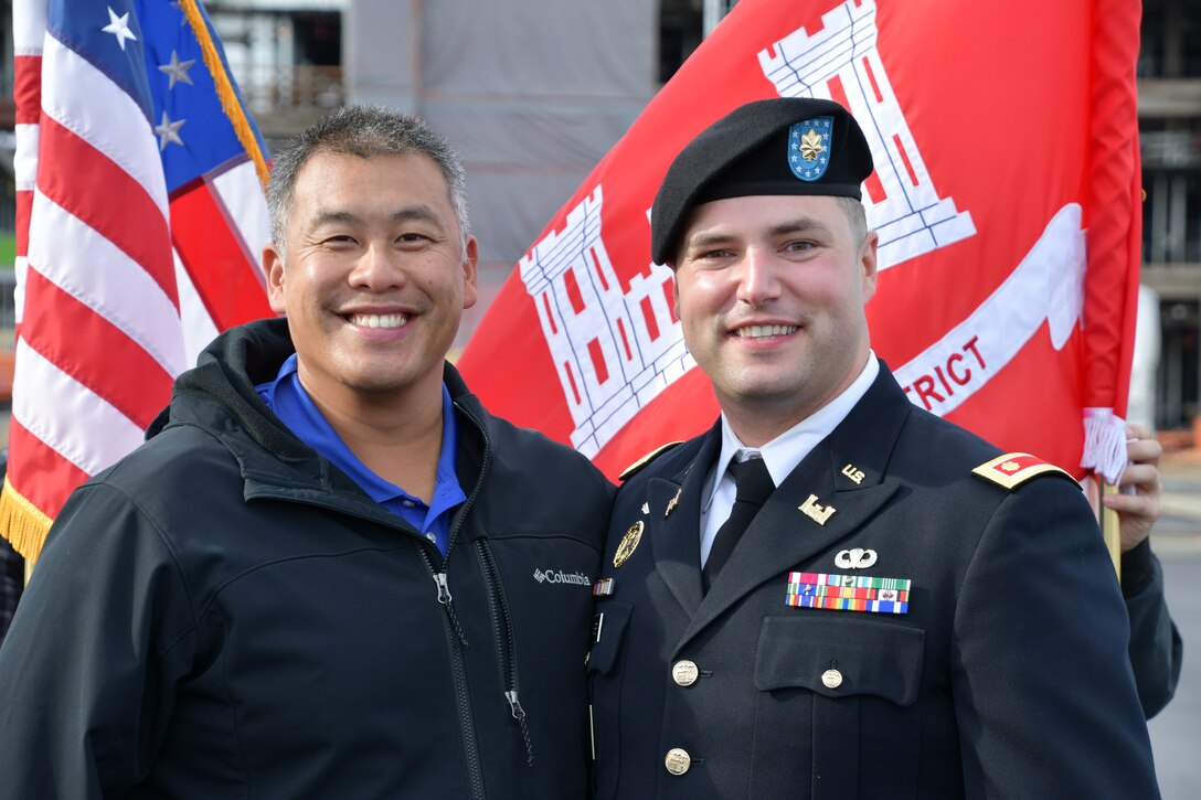 Two men pose for a picture in front of the American and USACE flags