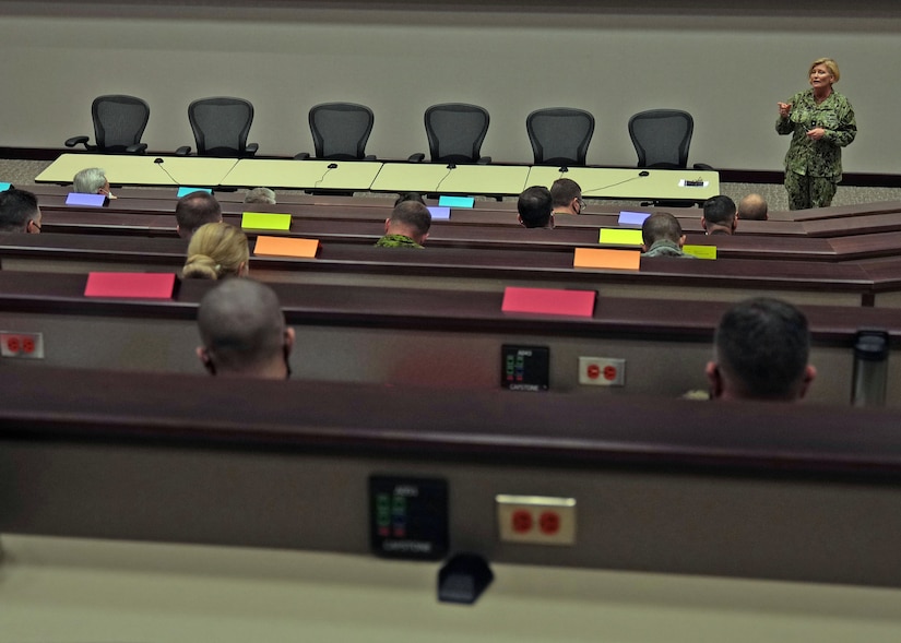 A female service member speaks to an audience in a meeting room.