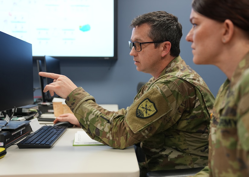 Two service members, one male and one female, look at a computer monitor.