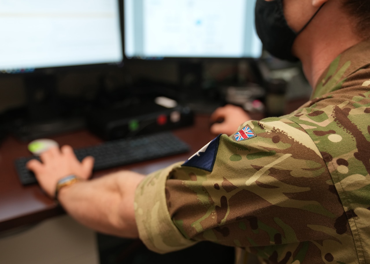 A service member with a patch of the British flag types on a computer's keyboard.
