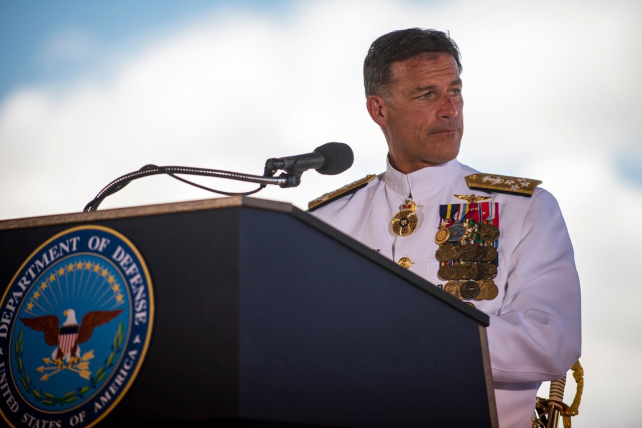 A Navy officer in dress uniform gives a speech from a lectern.