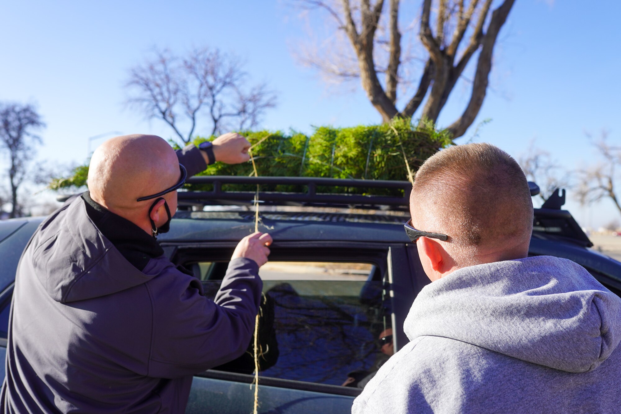 Volunteers tie a tree to the roof of a car during a Christmas tree giveaway event at Hill Air Force Base, Utah, Dec. 4, 2021. Trees for Troops, a program of the Christmas SPIRIT Foundation, provided live Christmas trees to 150 service members and their families with the help of volunteers from Hill AFB. (U.S. Air Force photo by 2nd Lt. Taylor Ferry)