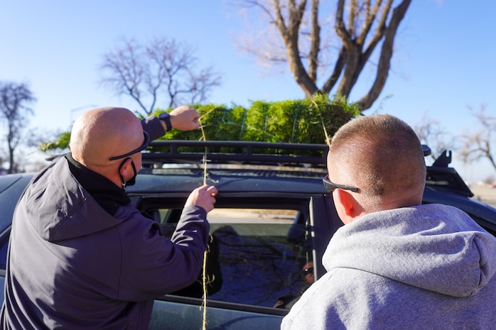 Volunteers tie a tree to the roof of a car during a Christmas tree giveaway event at Hill Air Force Base, Utah, Dec. 4, 2021. Trees for Troops, a program of the Christmas SPIRIT Foundation, provided live Christmas trees to 150 service members and their families with the help of volunteers from Hill AFB. (U.S. Air Force photo by 2nd Lt. Taylor Ferry)