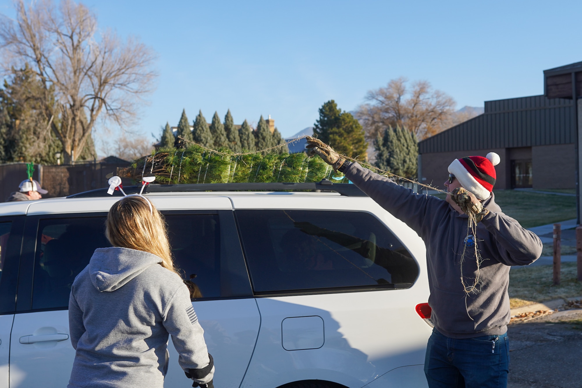 Volunteers tie a tree to the roof of a car during a Christmas tree giveaway event at Hill Air Force Base, Utah, Dec. 4, 2021. Trees for Troops, a program of the Christmas SPIRIT Foundation, provided live Christmas trees to 150 service members and their families with the help of volunteers from Hill AFB. (U.S. Air Force photo by 2nd Lt. Taylor Ferry)