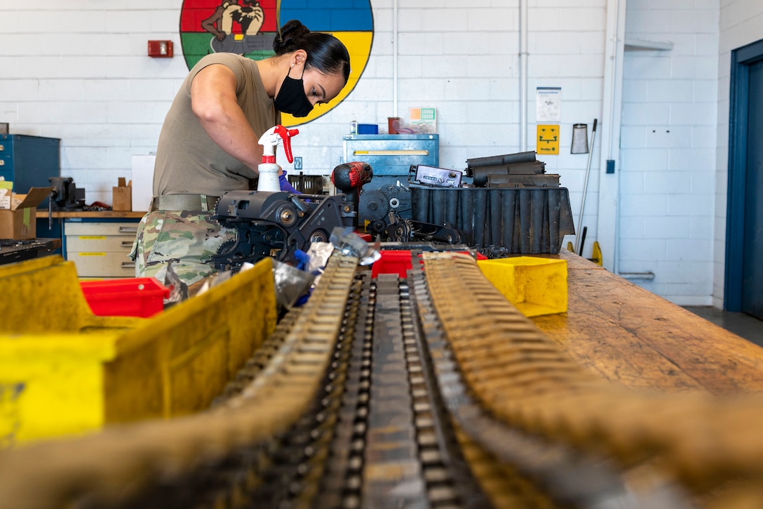 An airman cleans parts of a weapon in a shop.