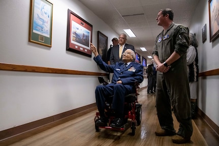 Man in motorized chair being given a tour by a pilot in military flight suit.