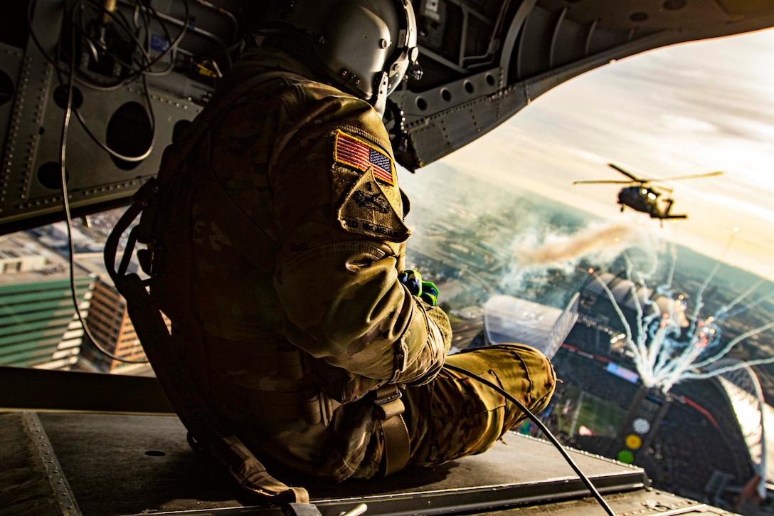 A soldier watches fireworks and a helicopter from the back of another aircraft.