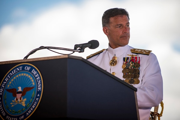 A Navy officer in dress uniform gives a speech from a lectern.