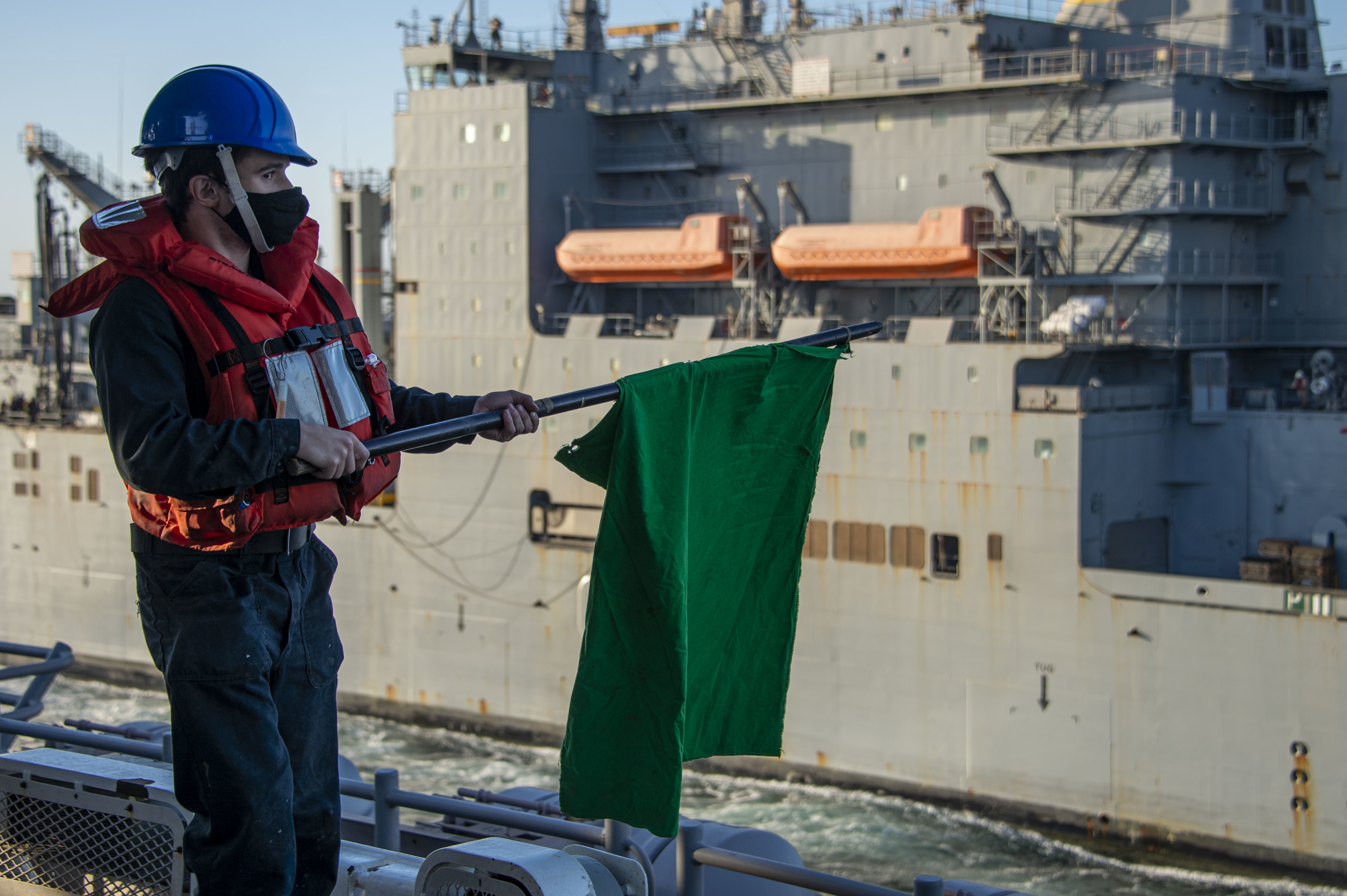 Seaman David Kats signals to dry cargo and ammunition ship USNS Wally Schirra (T-AKE 8) during a replenishment-at-sea aboard the amphibious assault ship USS Essex (LHD 2)
