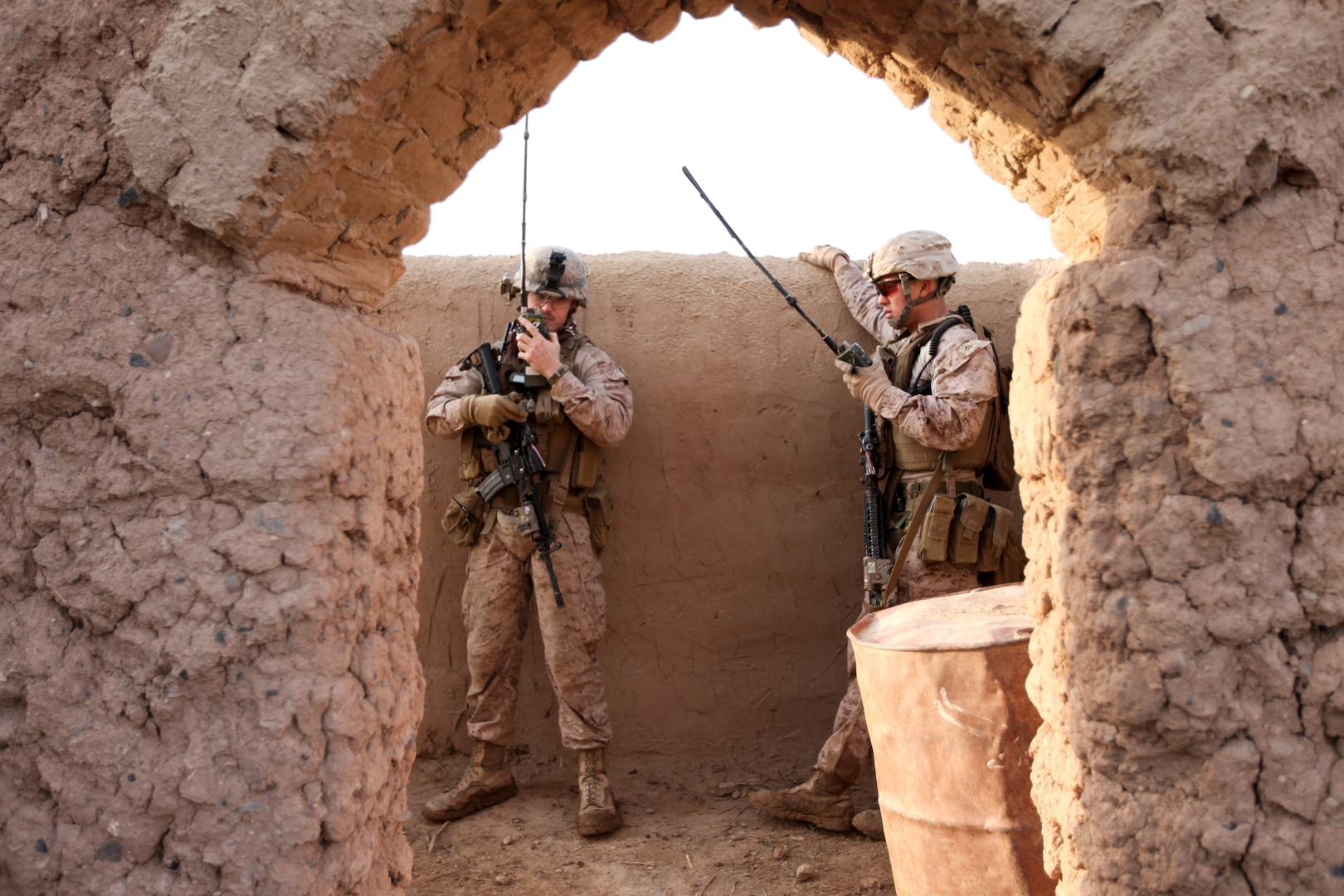 Two military personnel talk on hand-held radios.