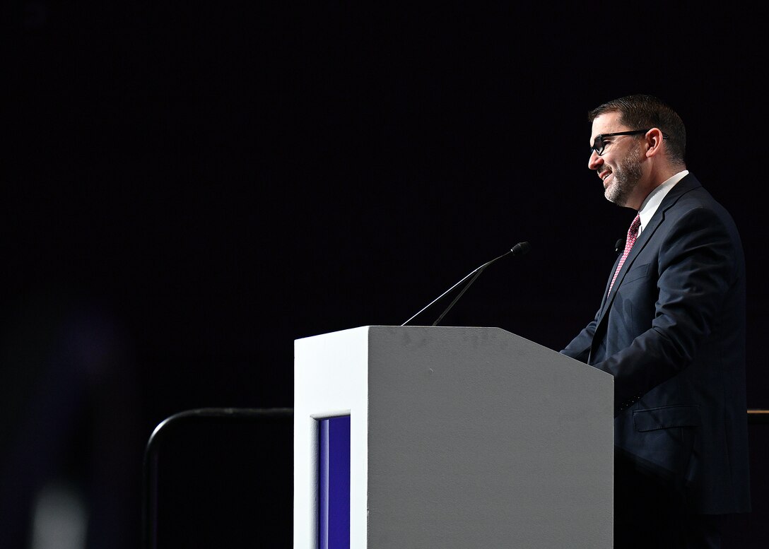 Image of a man on a stage behind a podium presenting to an audience.