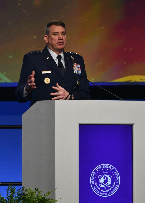Image of a man on a stage behind a podium. Speaking.