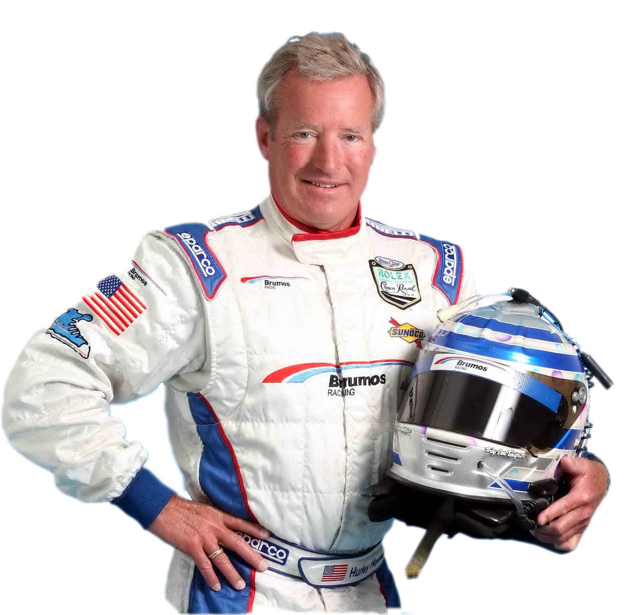 A race car driver poses for a picture in his racing suit, holding a racing helmet.