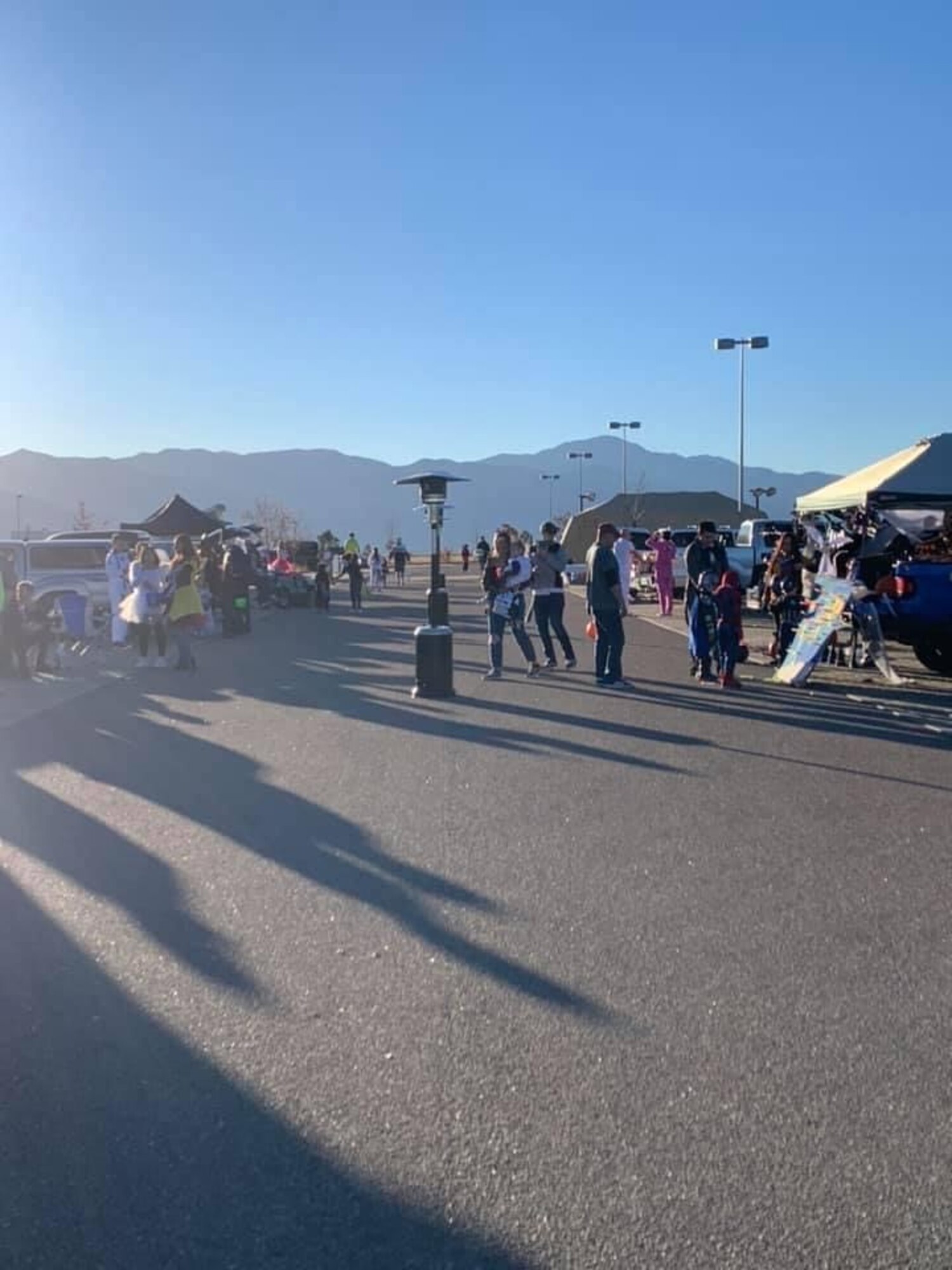 Family members gather around a street lined with cars for a trunk-or-treat event.