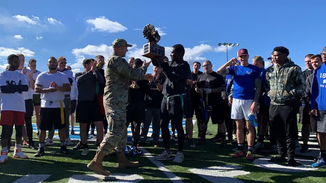military members and spouses gather around as the commander presents a trophy for the football game.