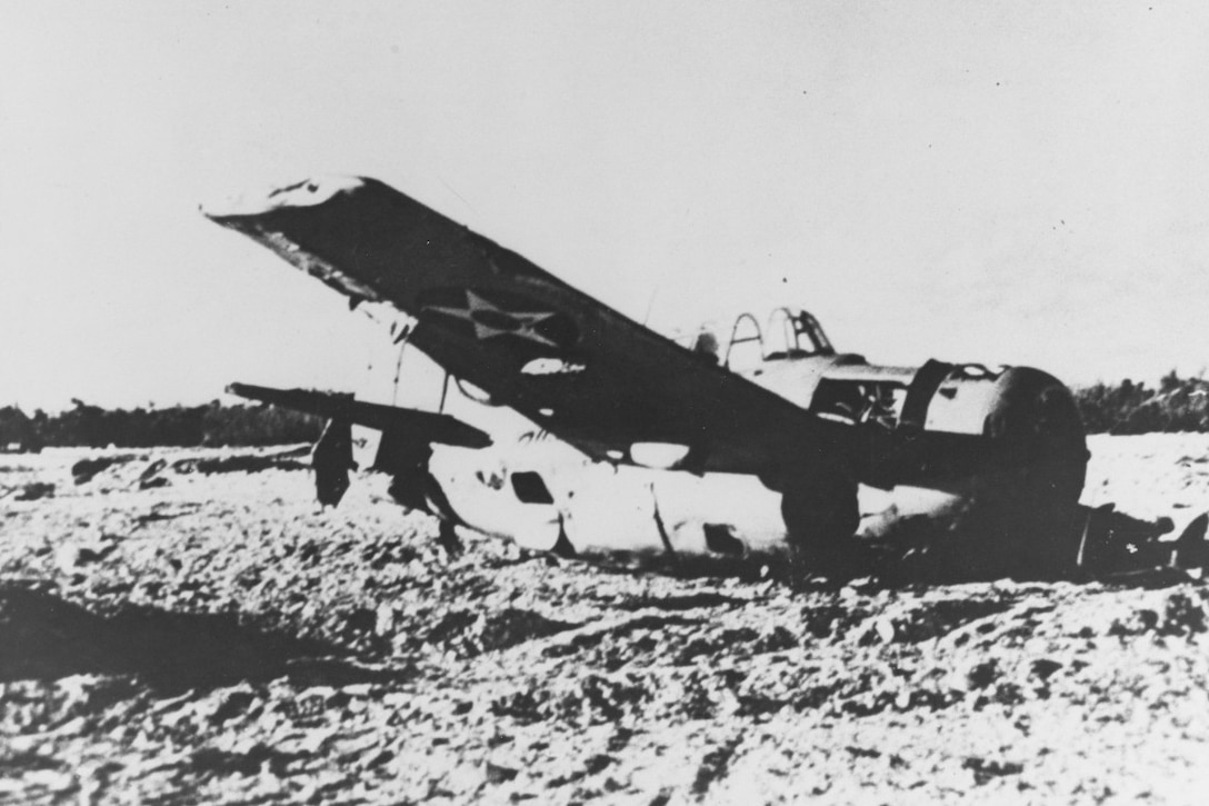 A propeller plane sits tilted in sand.