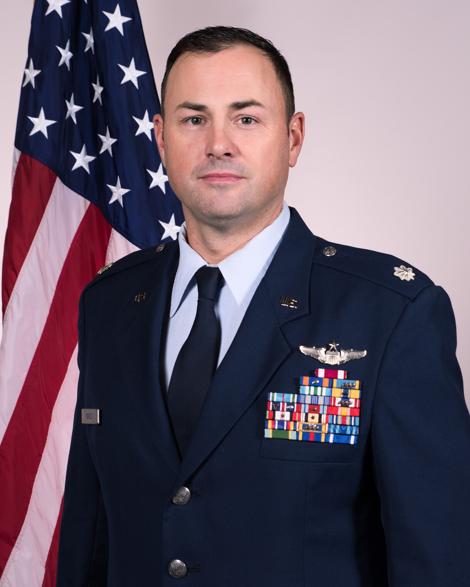Lt Col Kipp Parker official Air Force photo standing in dress uniform with American flag.