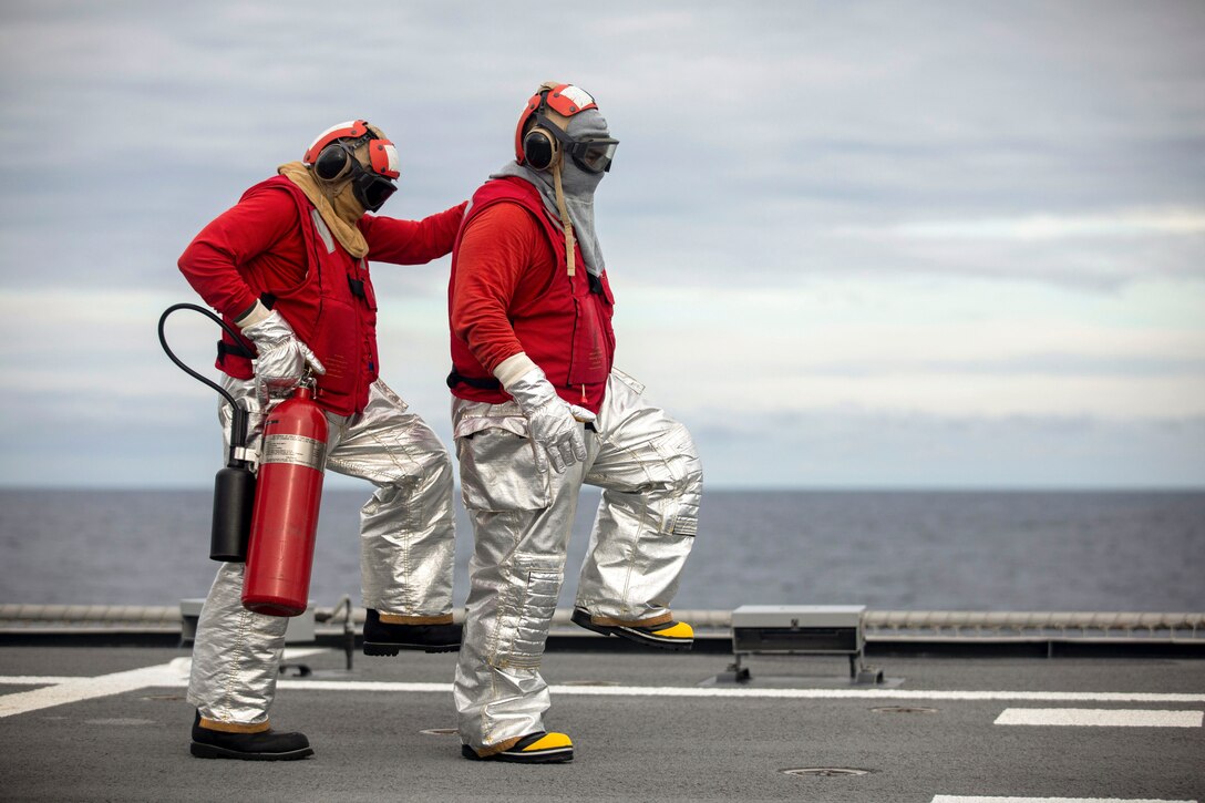 Sailors wearing protective fire gear step in formation during training on a ship at sea.