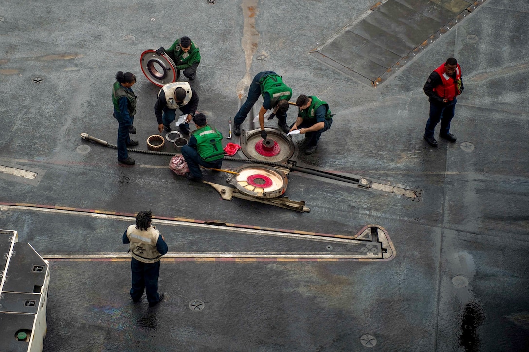 Sailors perform maintenance on a ship at sea.