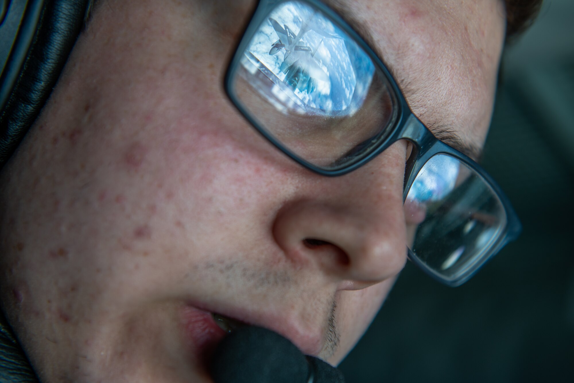 A boom operator's glasses catch the reflection of a fighter jet getting refueled by him