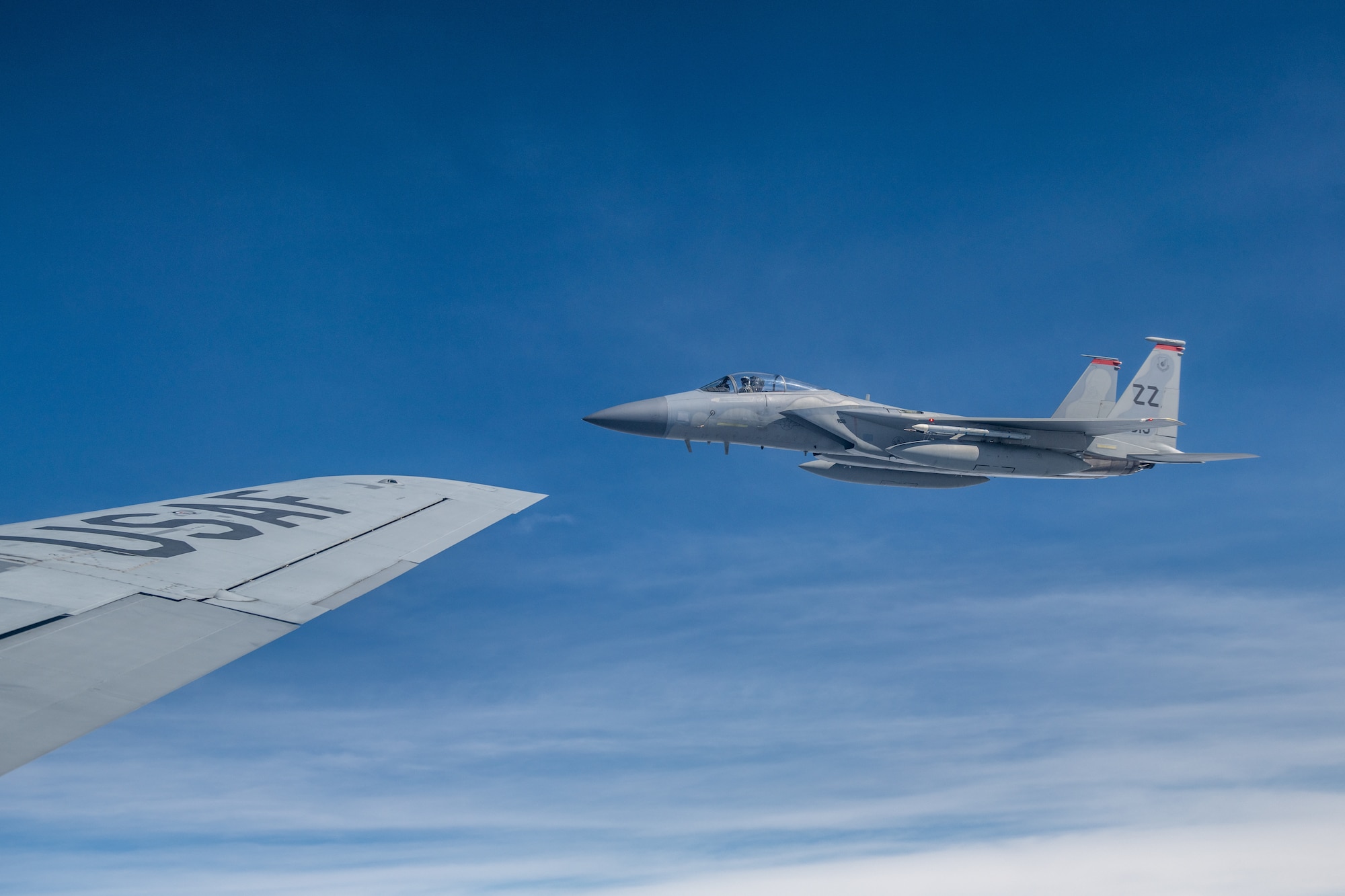 A fighter jet flies right next to the wing of KC-135 Stratotanker