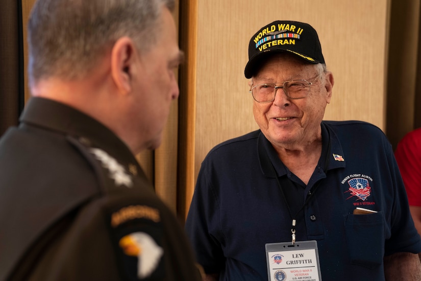 A man wearing a World War II veteran’s baseball-style cap speaks with a man in uniform.