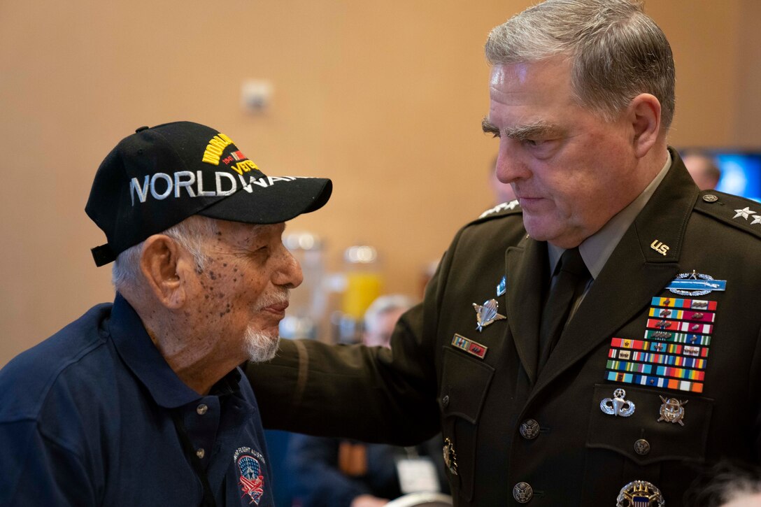 A man wearing a World War II veteran’s baseball-style cap speaks with a man in uniform.