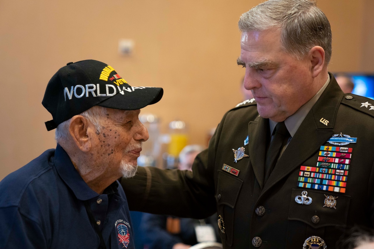 A man wearing a World War II veteran’s baseball-style cap speaks with a man in uniform.