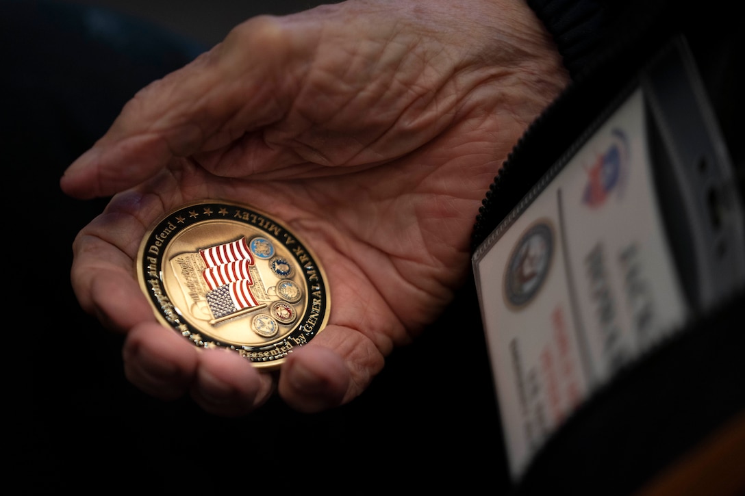 A wrinkled hand holds a challenge coin.